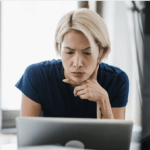 Person leaning over a laptop with a concerned, thoughtful expression while reviewing something online